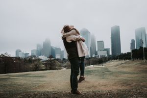 Two figures embrace in a close hug against the moody cityscape of skyscrapers on a cloudy winter day in Houston.