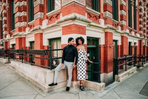 A couple poses at the corner of a historic red and white striped brick building with ornate architectural details.
