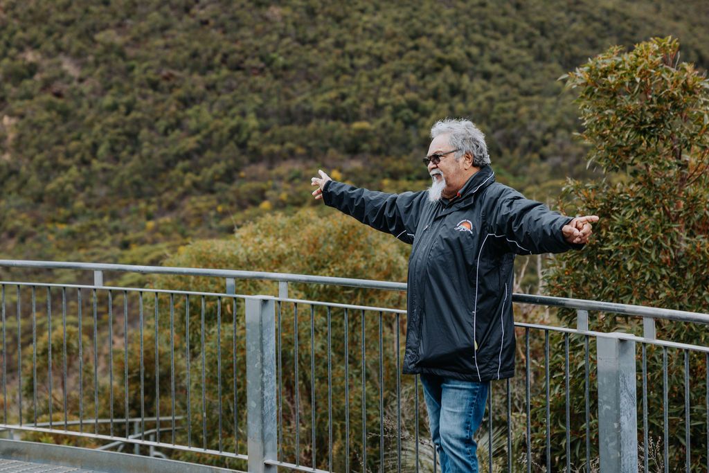 Person in dark jacket demonstrates gestures while standing on metal platform with mountain views.