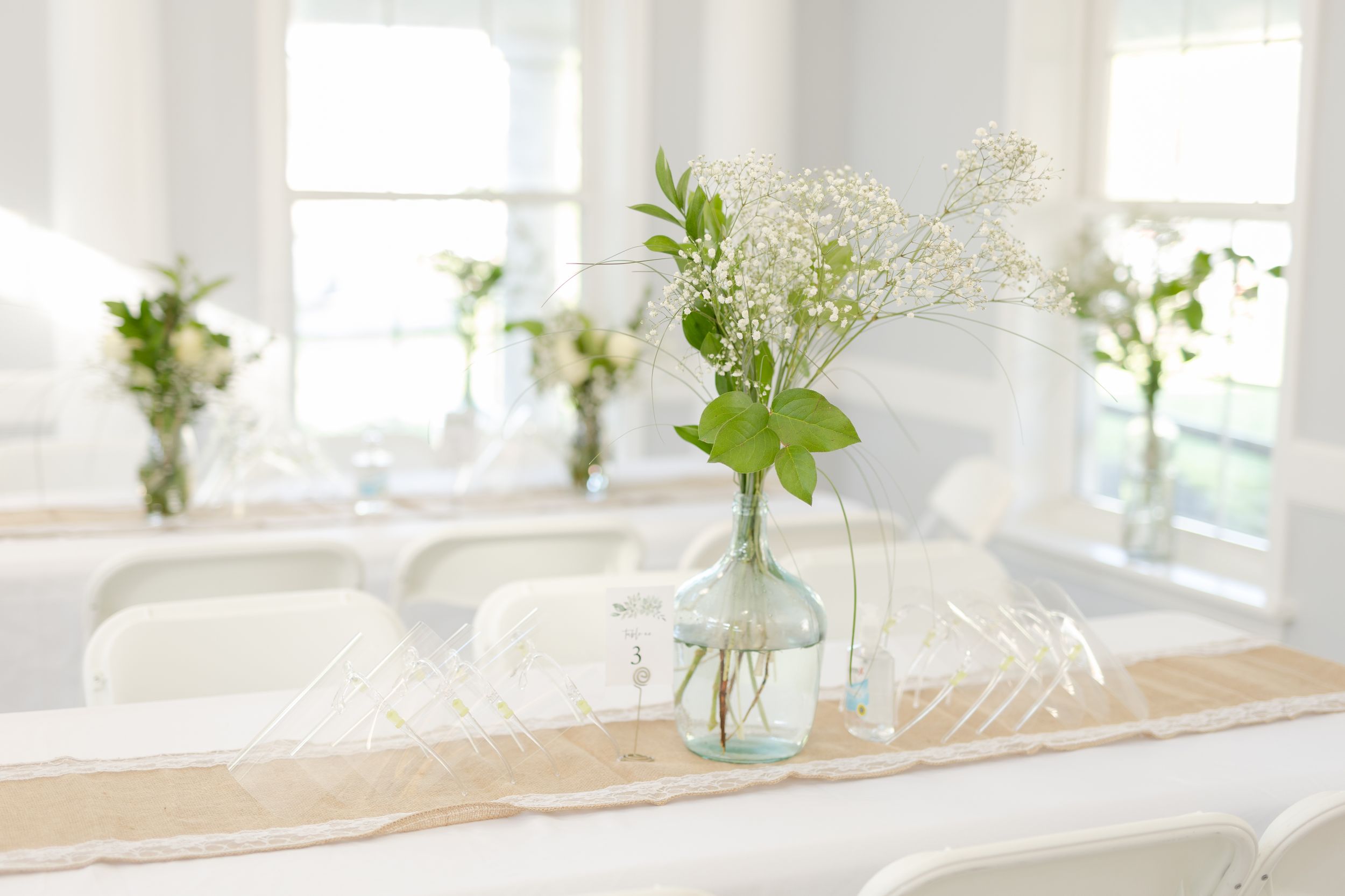 Simple glass jar centerpiece with delicate white flowers on a wooden table setting.