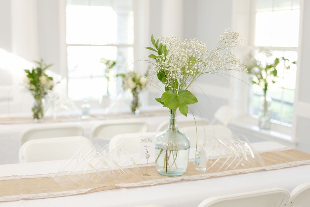 Simple glass jar centerpiece with delicate white flowers on a wooden table setting.