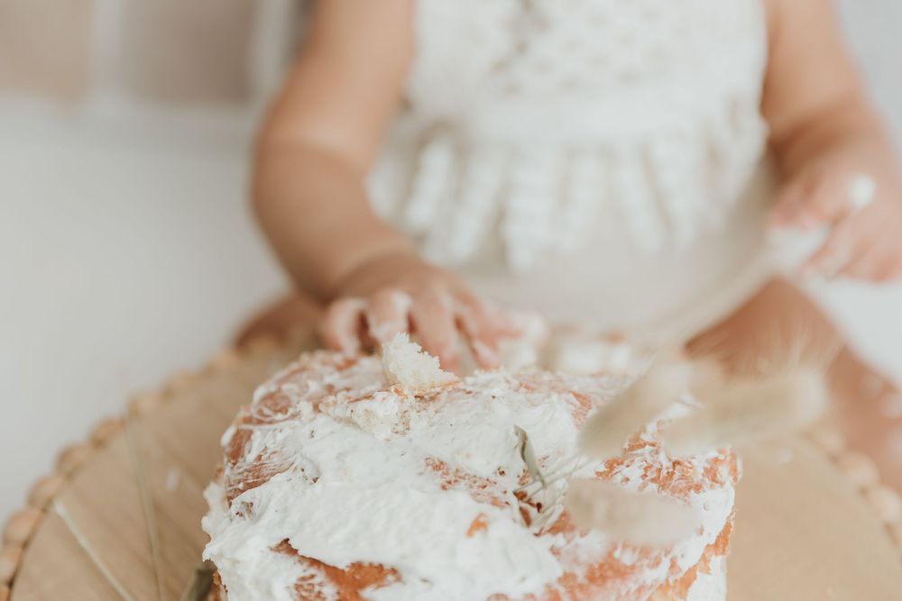 Close-up view of small hands playing with white frosting or cream on a wooden surface.