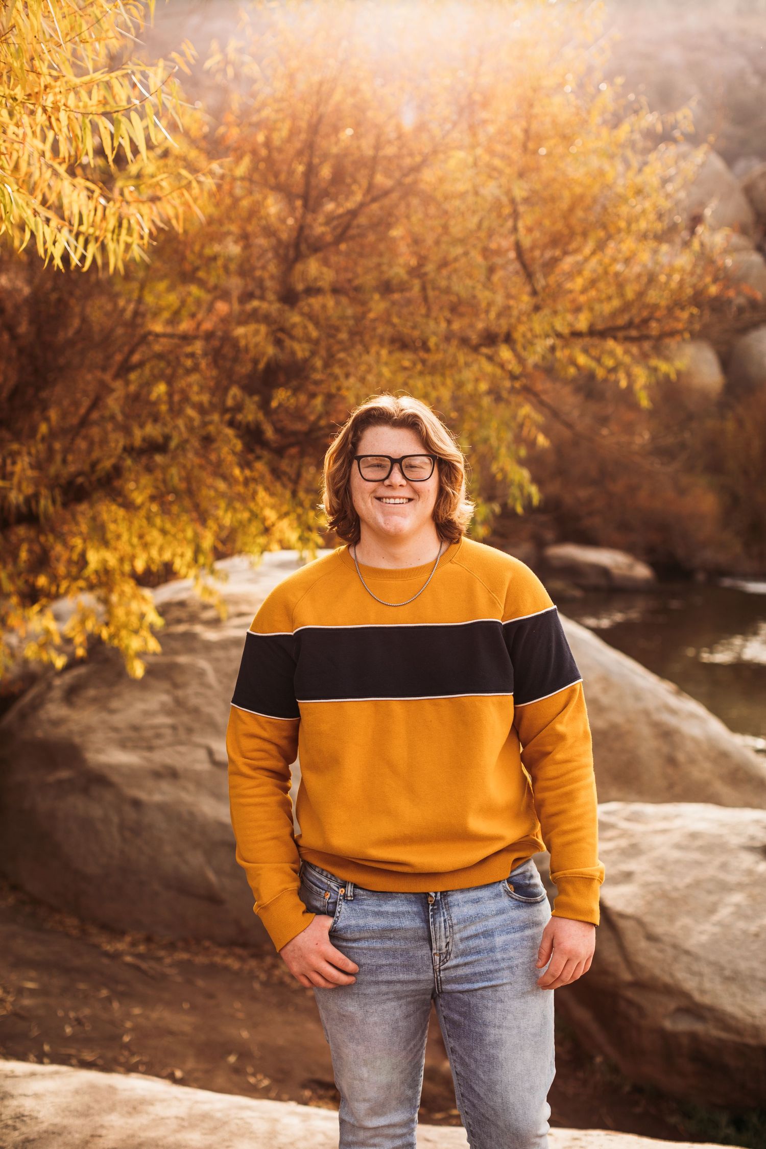 A casual portrait against autumn foliage with golden sunlight filtering through trees.