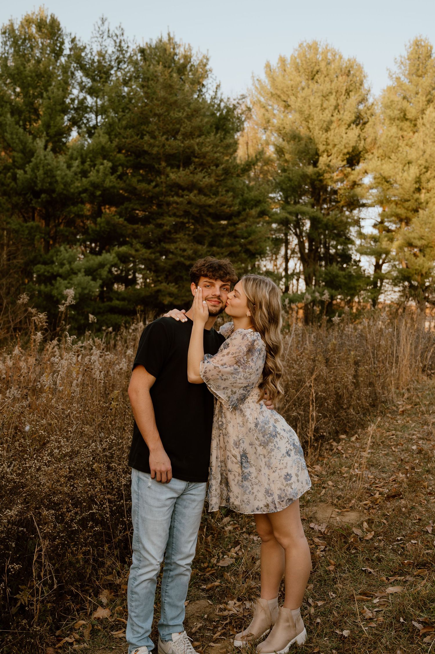 A romantic couple shares an intimate moment against a backdrop of pine trees at sunset.