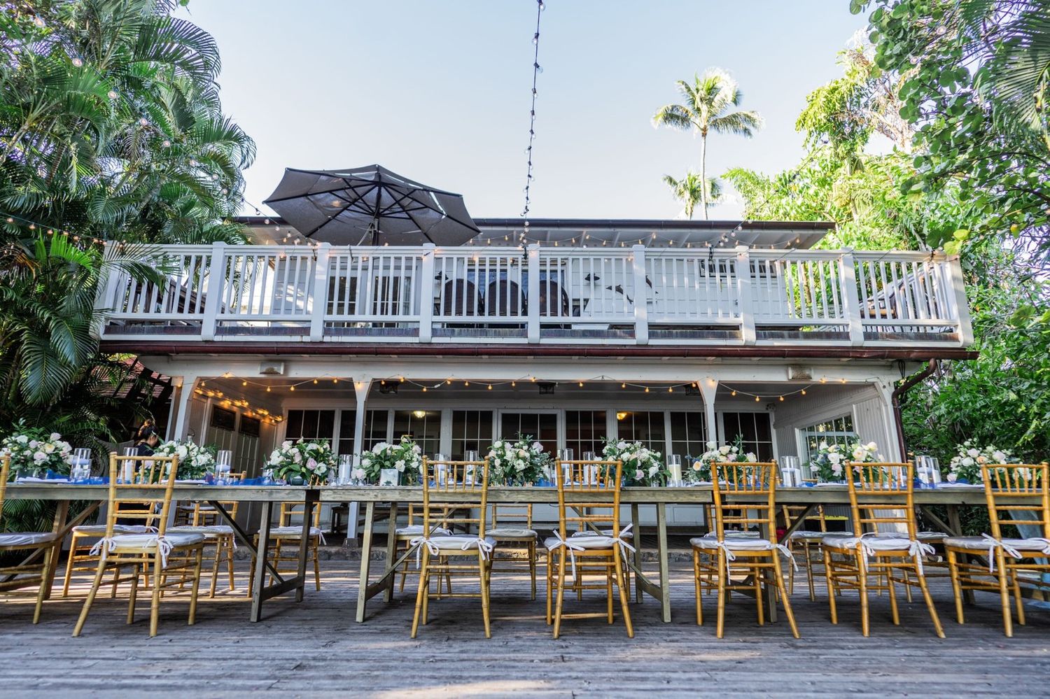 An outdoor wedding reception venue with long tables and gold chairs beneath a white balconied building.
ベイヤーエステートでプライベートウェディング

ぷ