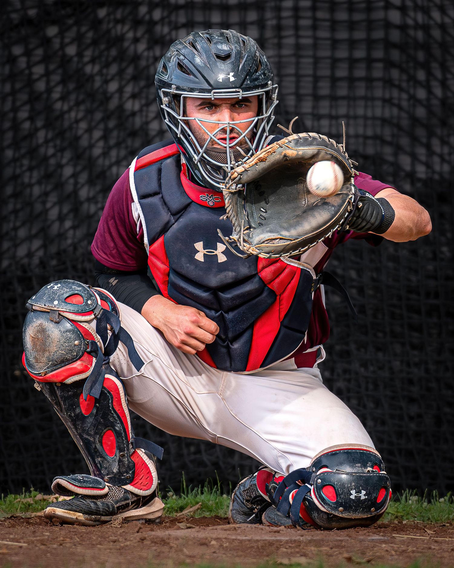Baseball catcher in protective gear crouches ready to catch behind home plate.