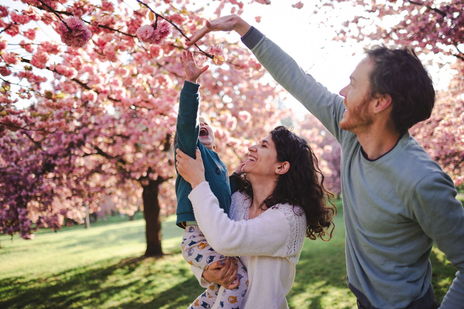Une famille portant des habits coordonnés aux tons doux et naturels joue dans un verger en fleurs