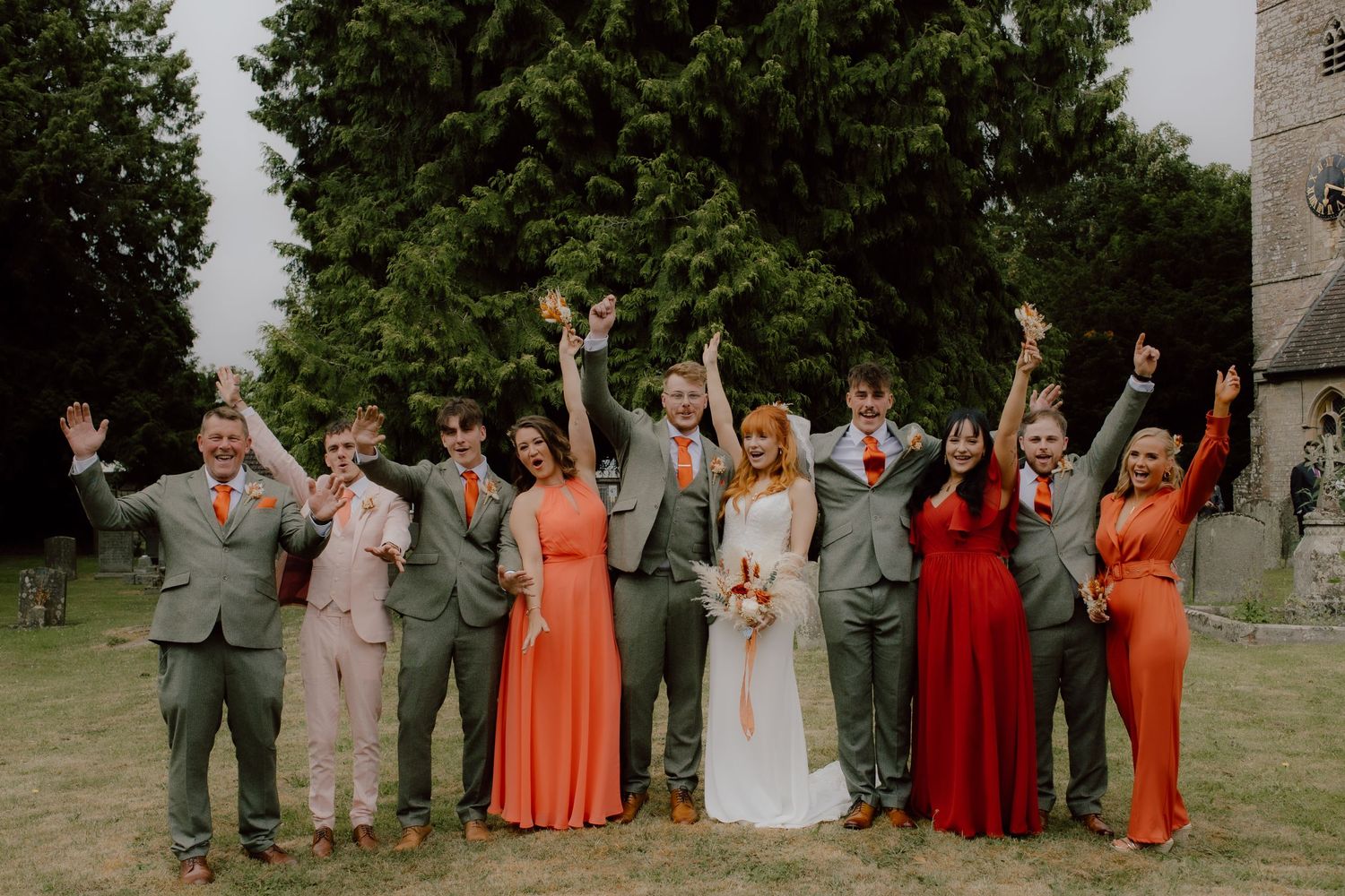 Wedding party celebrates with arms raised on a sunny outdoor lawn.