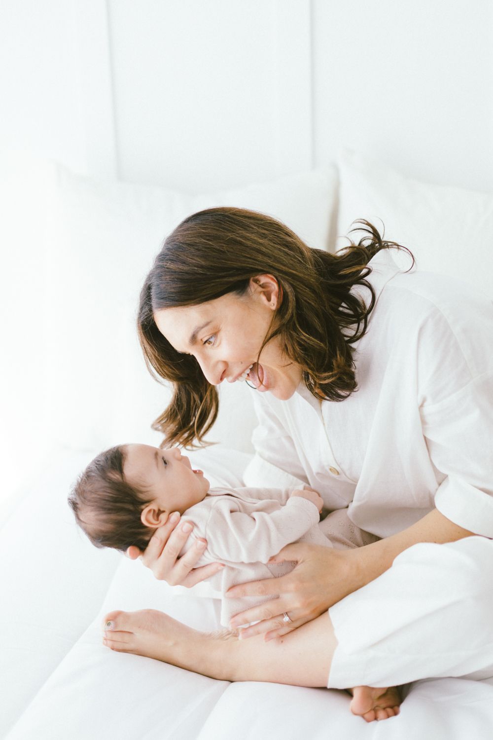 Loving interaction between parent and child on white bed in bright setting.