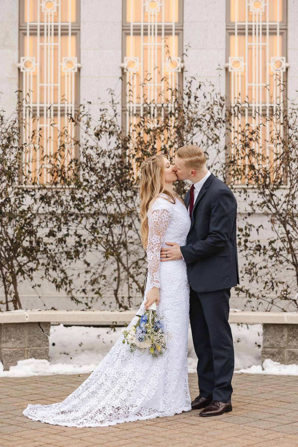 Couple in wedding attire share romantic moment against ornate building facade.