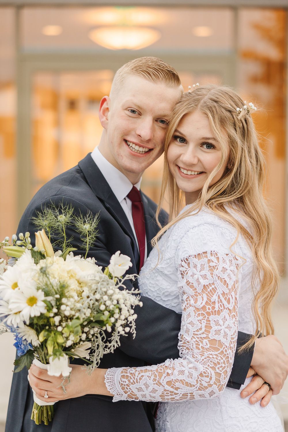 A wedding photo of a couple in formal attire with a bouquet of white daisies and baby's breath.