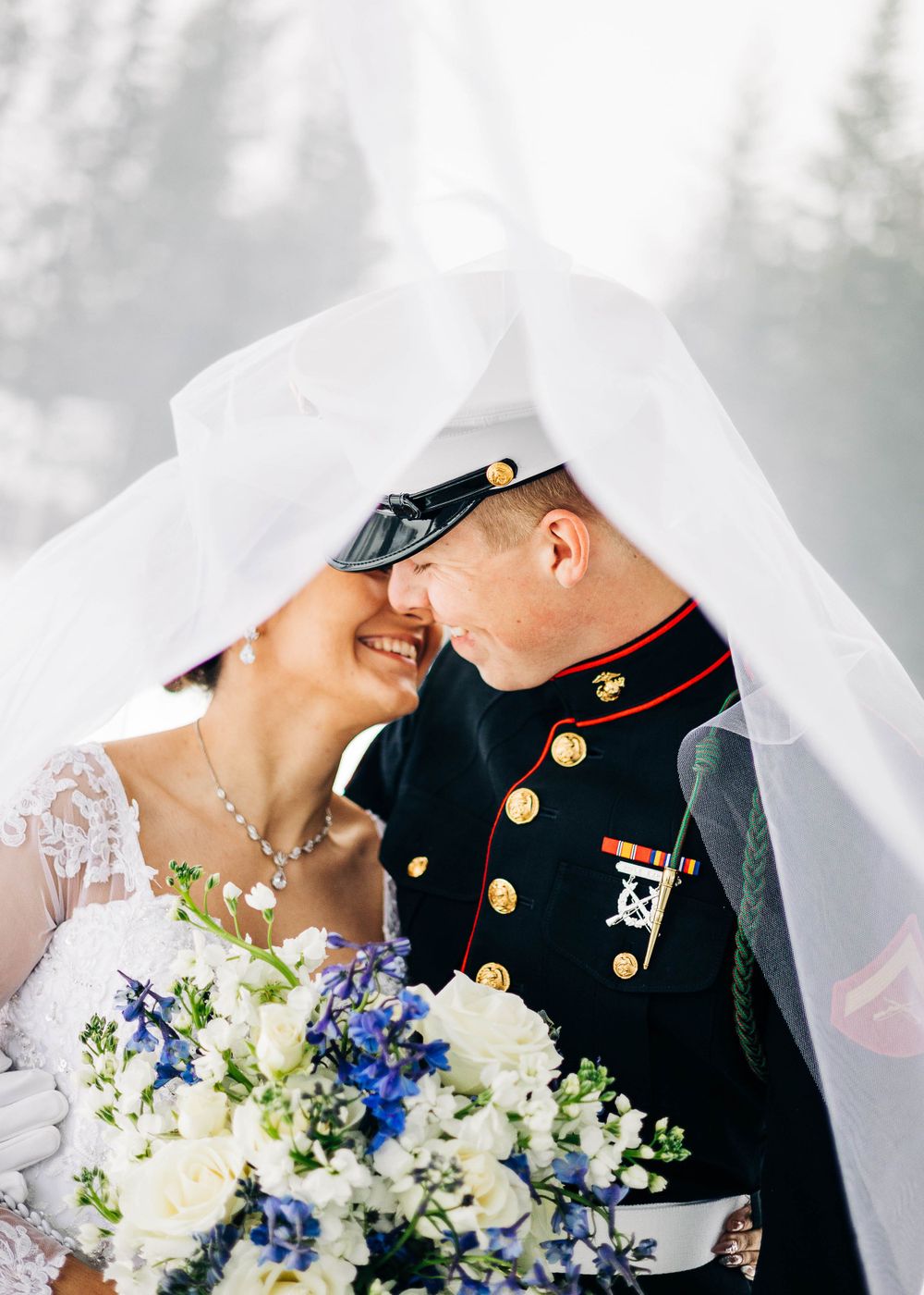 A tender wedding moment under a flowing veil with a bouquet featuring white and blue flowers.