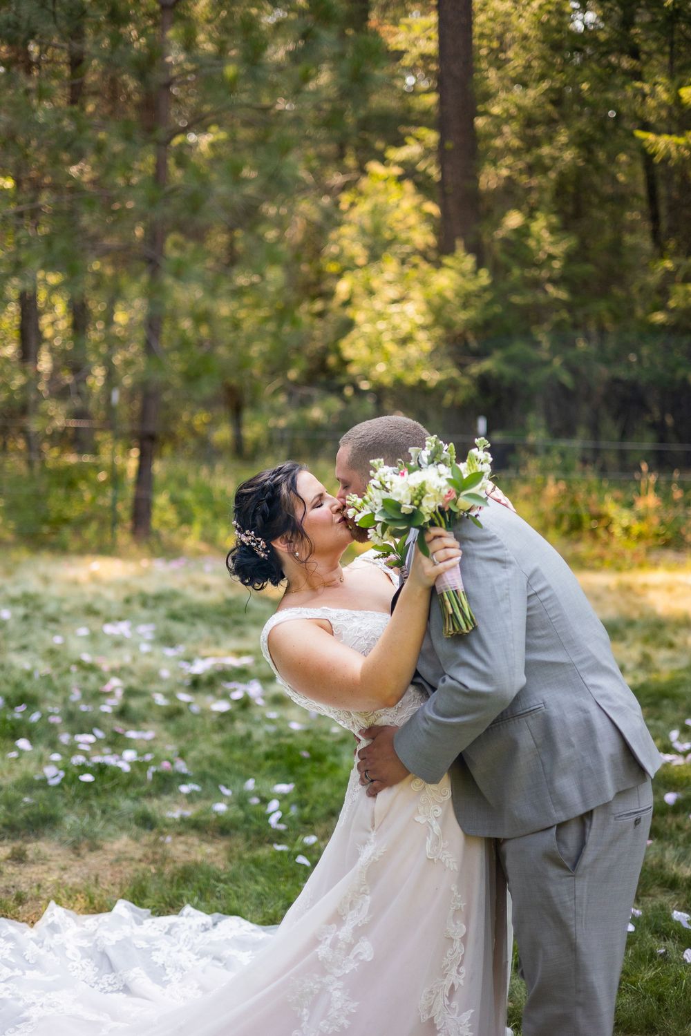 Playful wedding portrait in a sunlit forest with white floral bouquet.