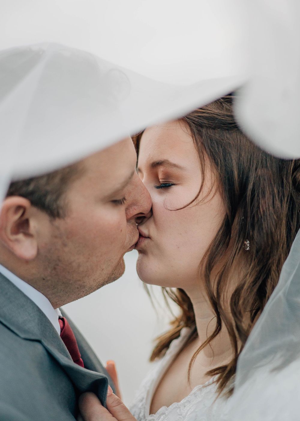 Intimate wedding photo under a sheer veil with soft lighting.