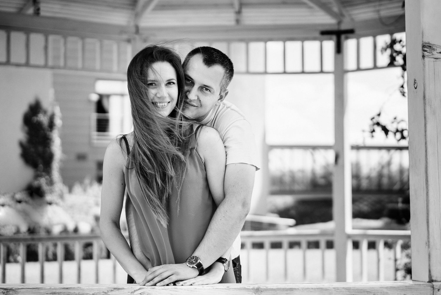 Black and white photo of a couple embracing on a bright sunlit porch.