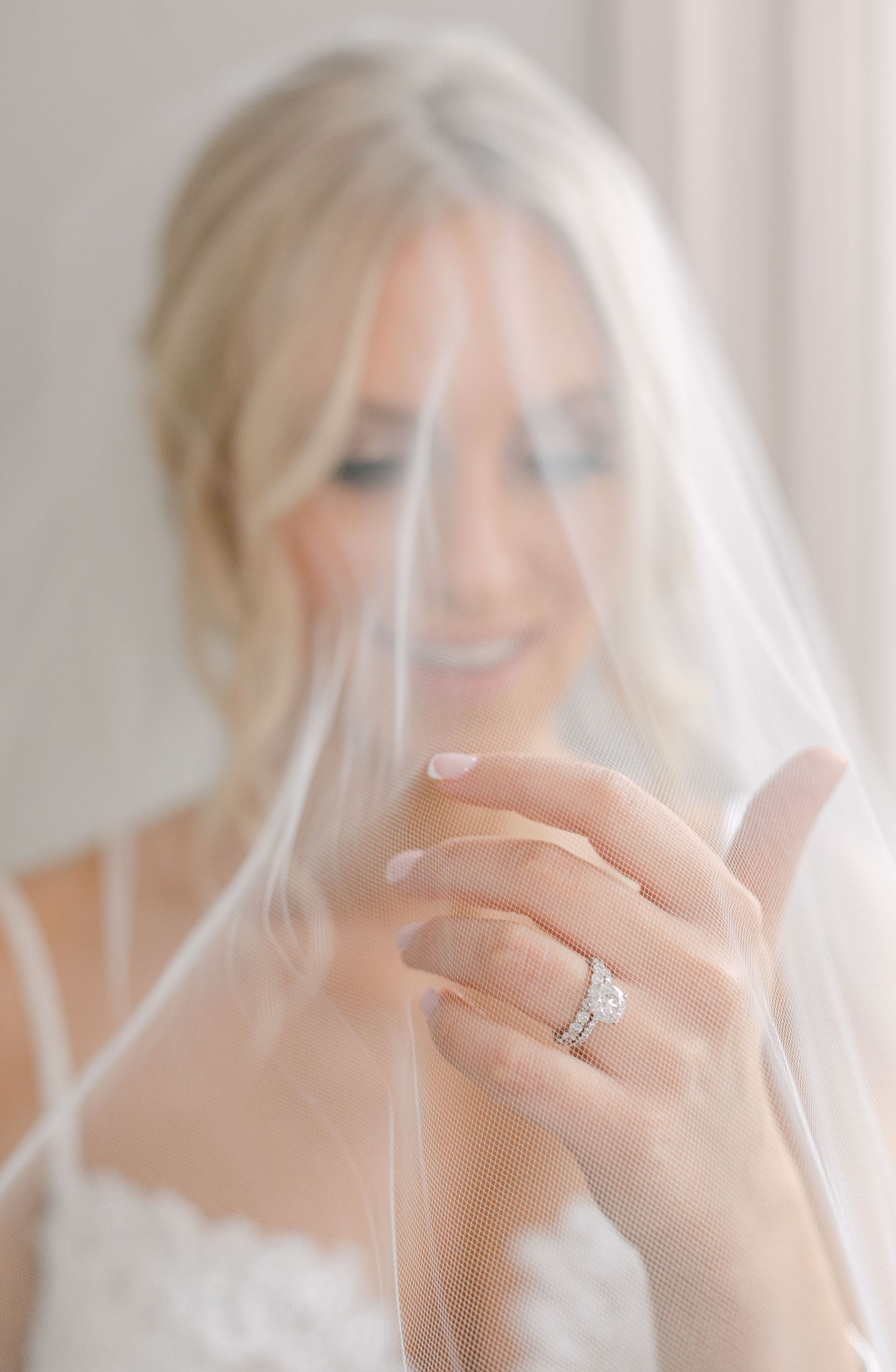 Close-up of bride's hand showing engagement ring through delicate veil.