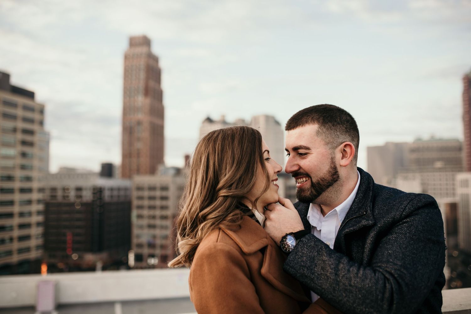 A romantic moment between a couple on a city rooftop with downtown buildings in the background.