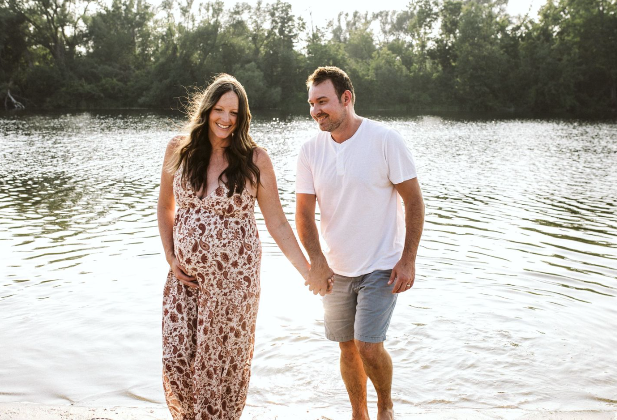 A couple holding hands while walking along a serene lakeside at sunset.