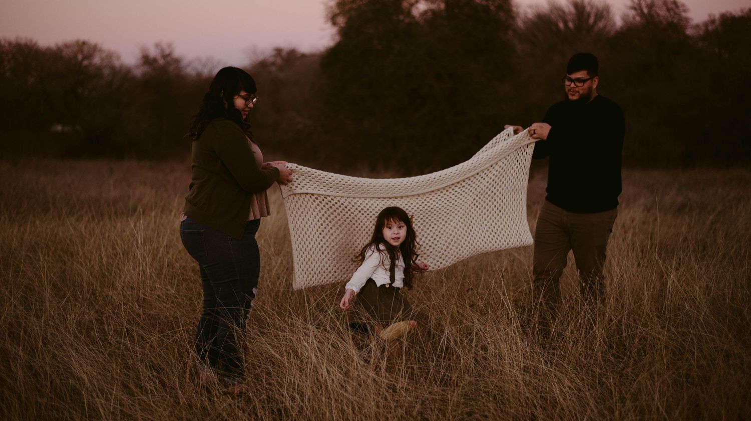 Family holding white sheet in field during sunset photoshoot.