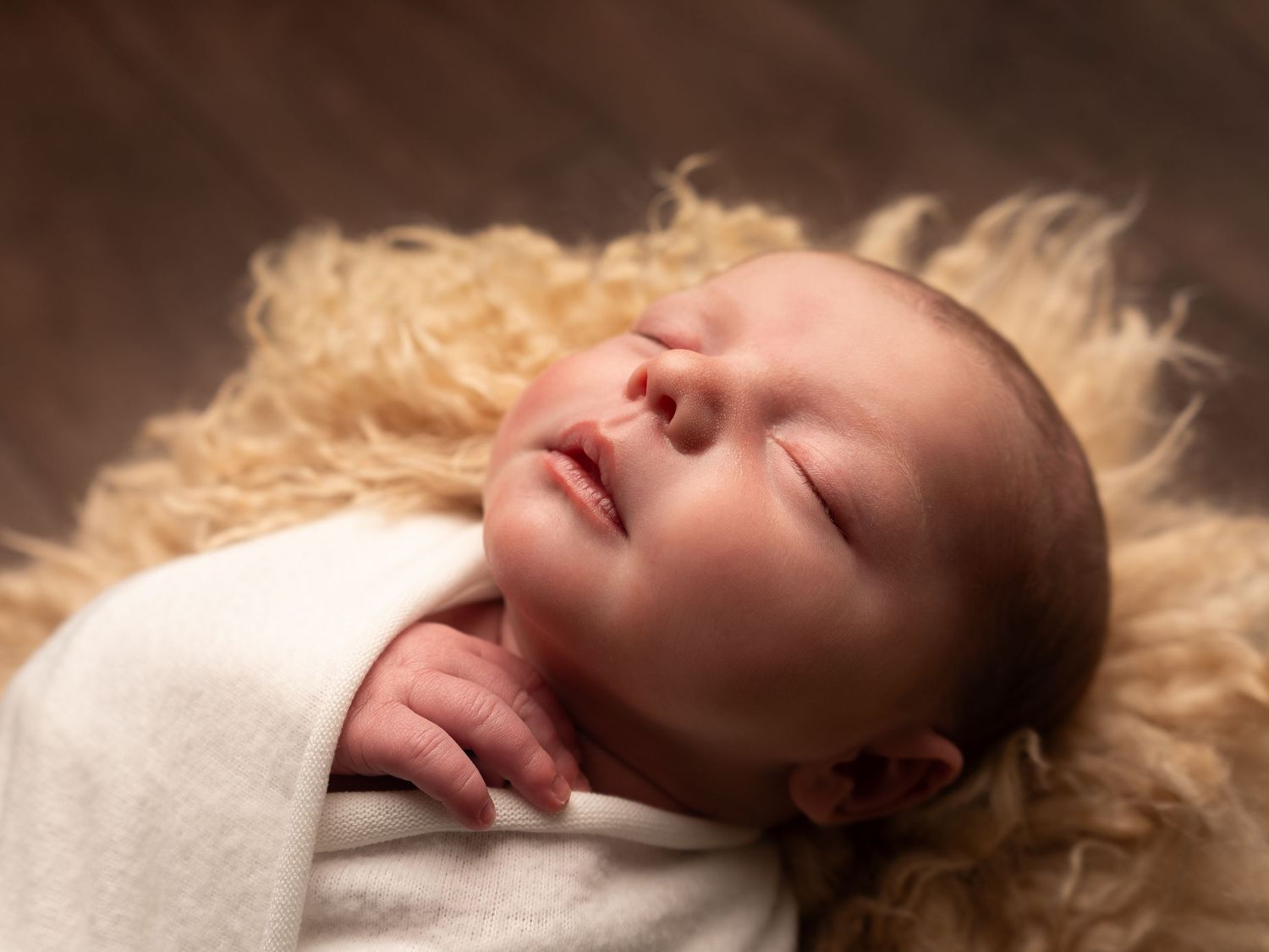 baby boy close up wrapped in white in a fluffy basket by professional newborn photographer in Doncaster.