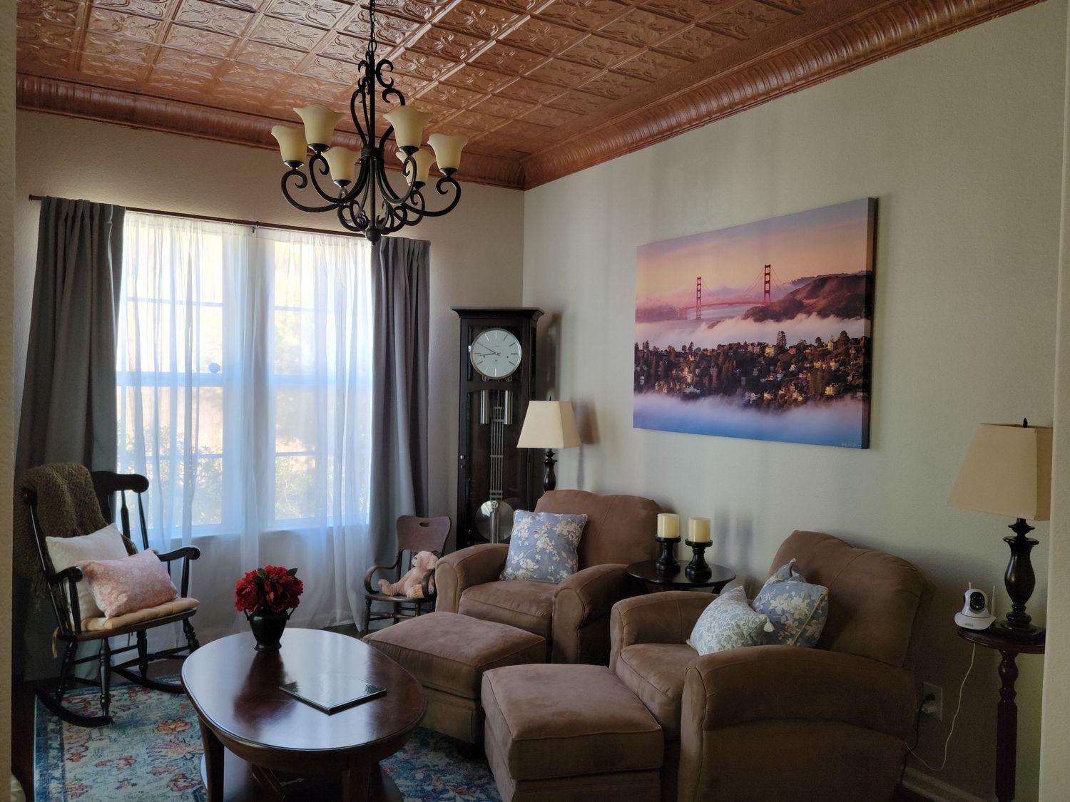 Cozy living room with brown recliners, chandelier, winter landscape artwork, and ornate tin ceiling.