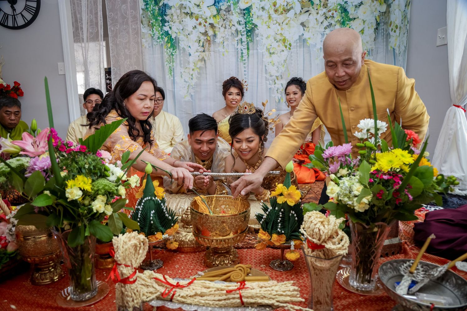 A family gathering around a traditional ceremony table with colorful flowers and decorative elements.