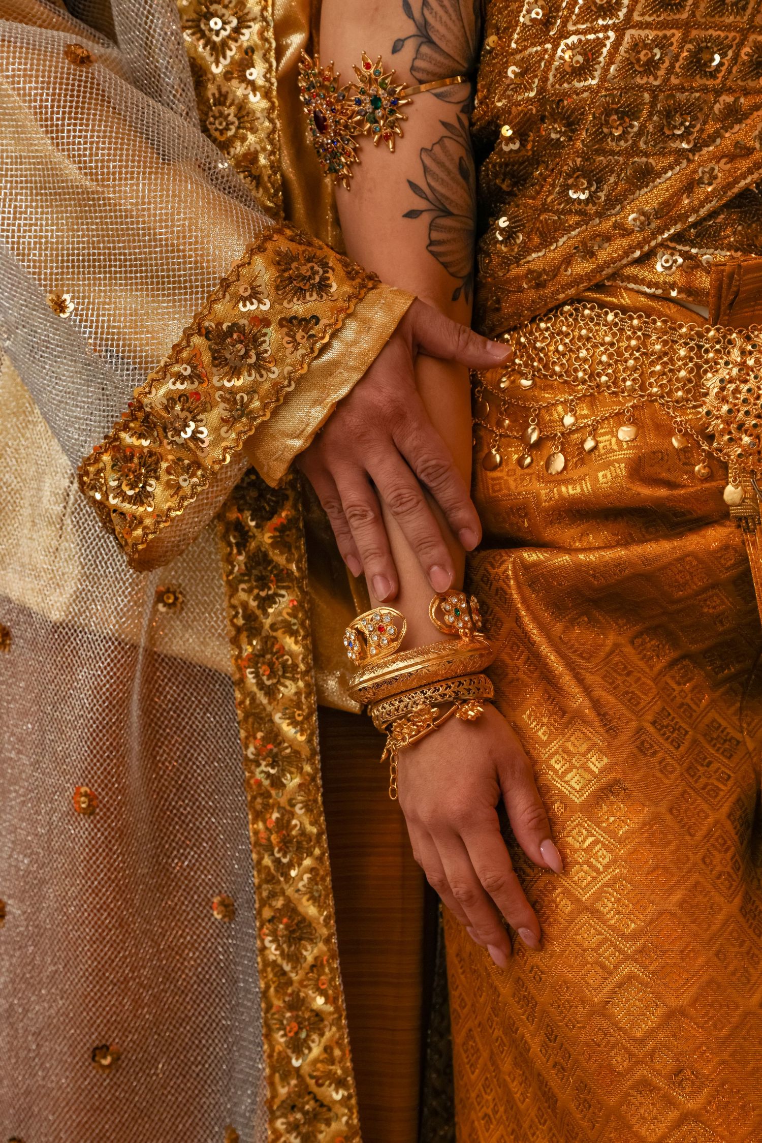 Close-up of ornate gold embroidered wedding attire with hands showing delicate jewelry details.