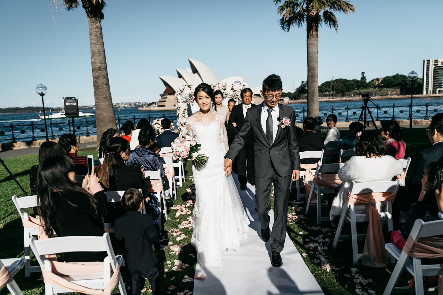 Bride and groom walk down the aisle at an outdoor Sydney Opera House wedding ceremony.