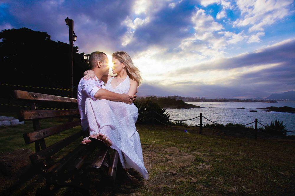 A romantic sunset photoshoot by a lighthouse with dramatic purple clouds over the ocean.