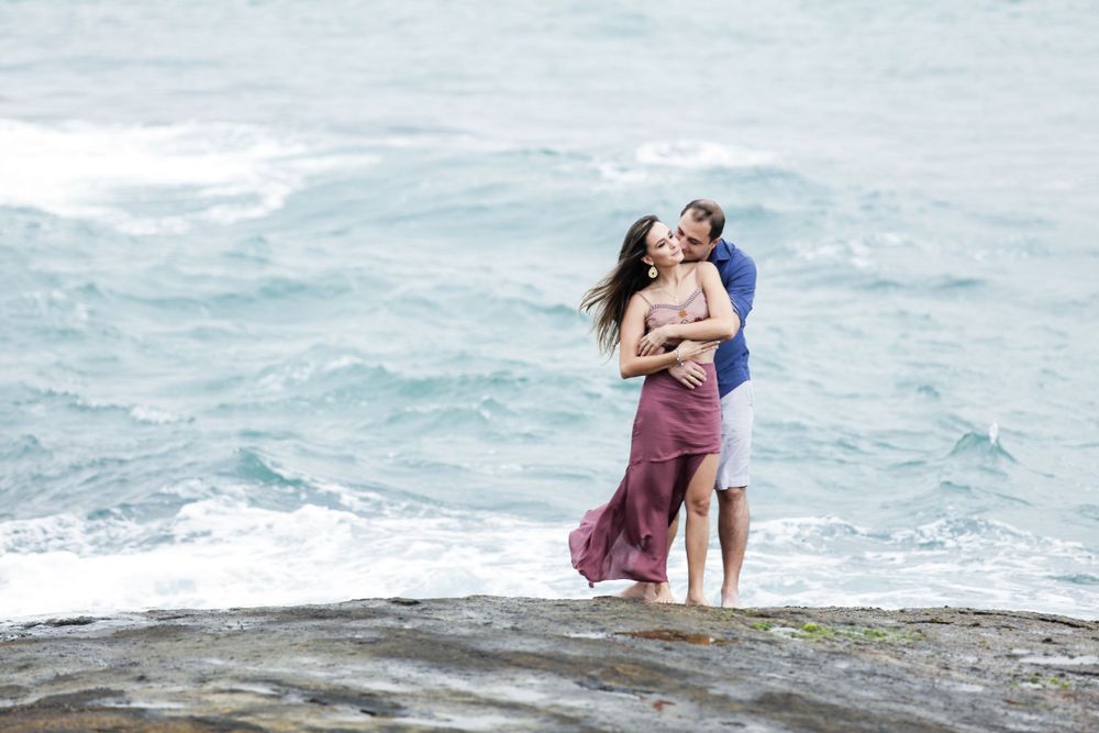 A couple embraces on rocky shore with crashing waves in the background.