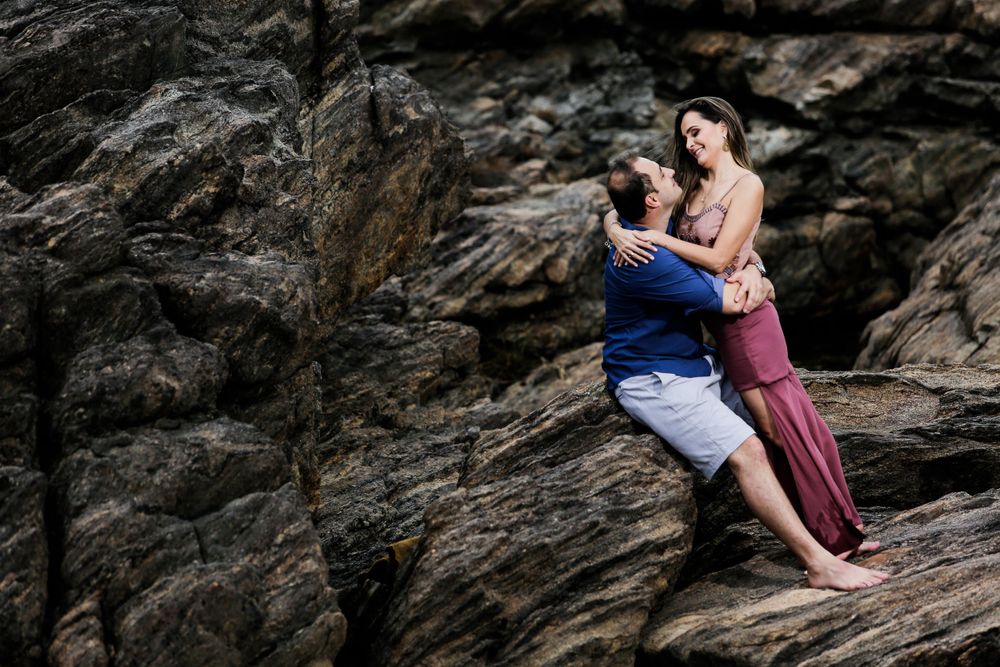 A couple poses intimately on dark rocky cliffs by the ocean.
