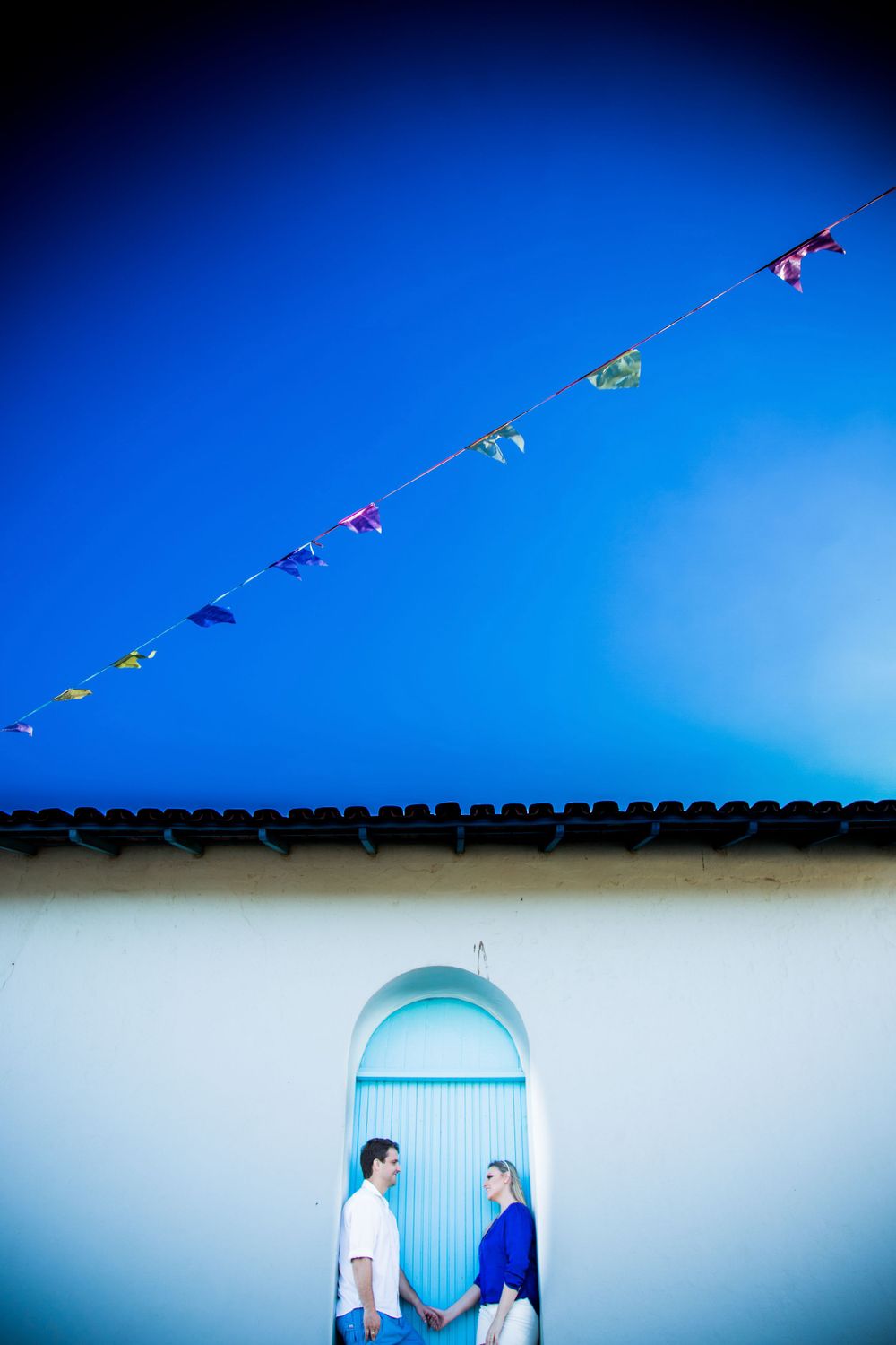 A couple holds hands under a blue archway with colorful flags strung overhead.