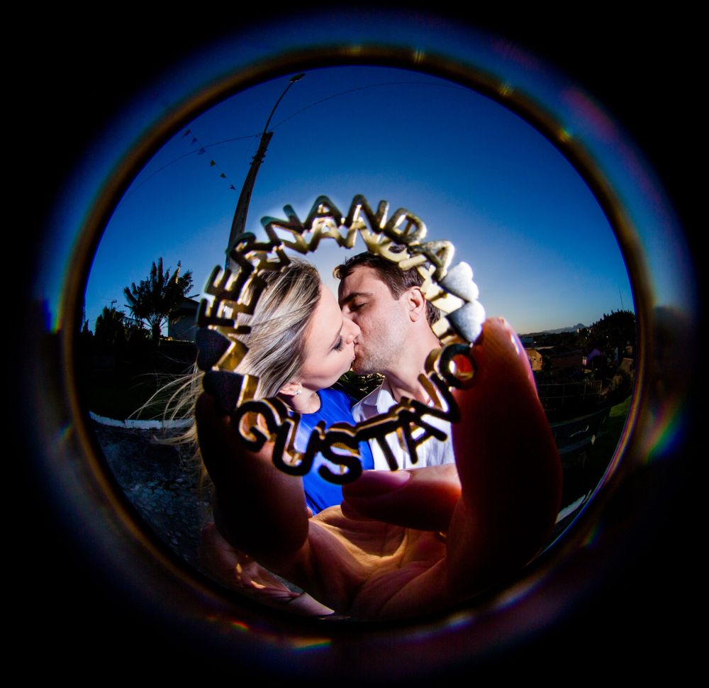 A circular fisheye lens captures a couple's intimate moment against a blue sky background.