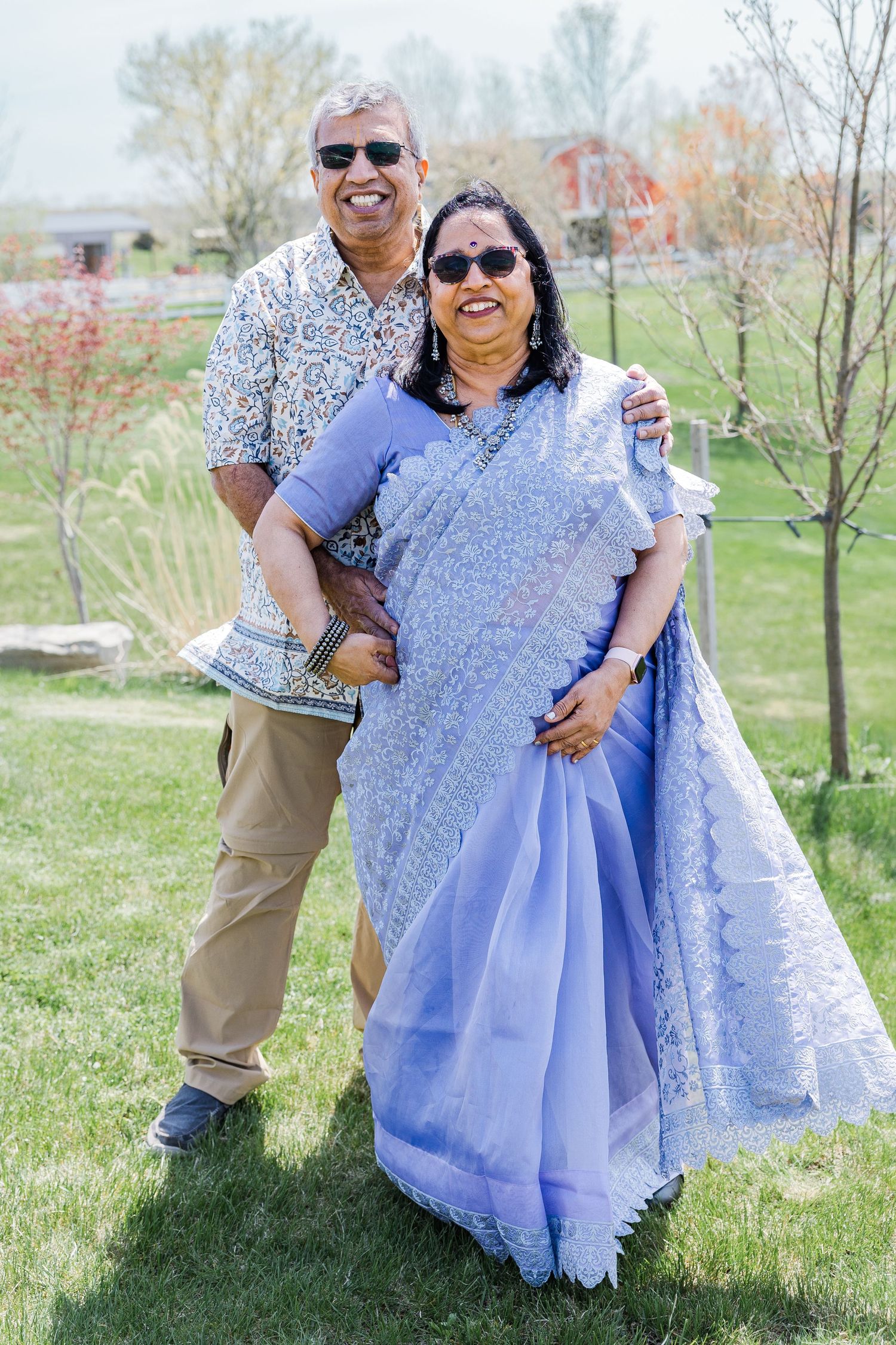A couple poses outdoors in spring, wearing traditional Indian and casual western attire.
