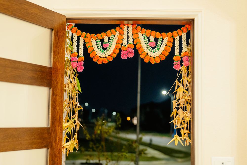 Traditional Indian toran decoration with orange and black flower garlands hangs above a doorway at night.