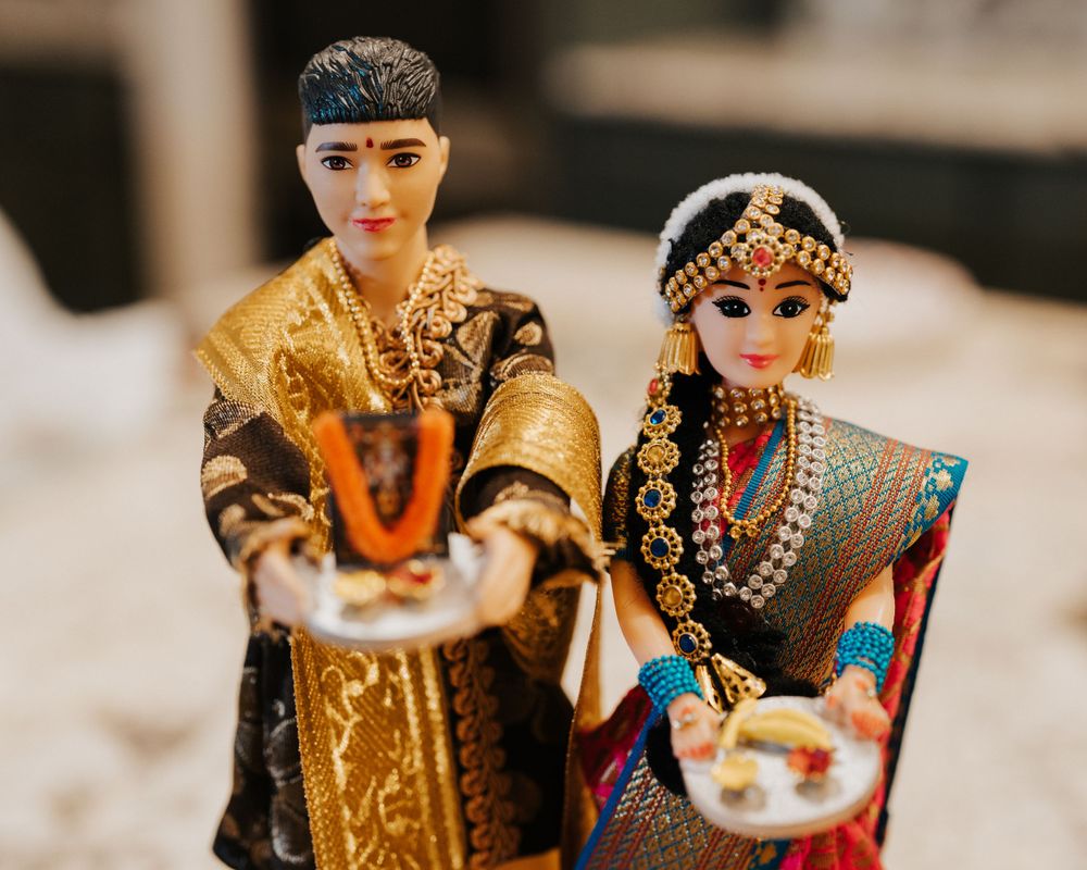 Decorative dolls wearing traditional Indian wedding attire holding ceremonial items.
