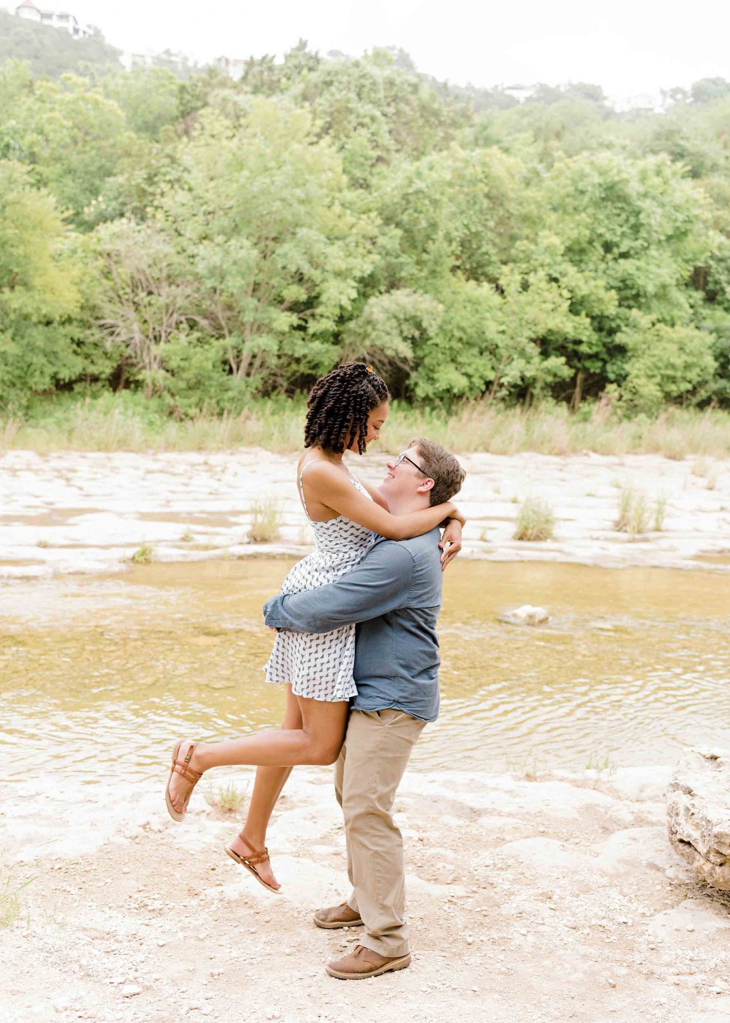 Joyful couple sharing a playful lift moment by a scenic riverside.