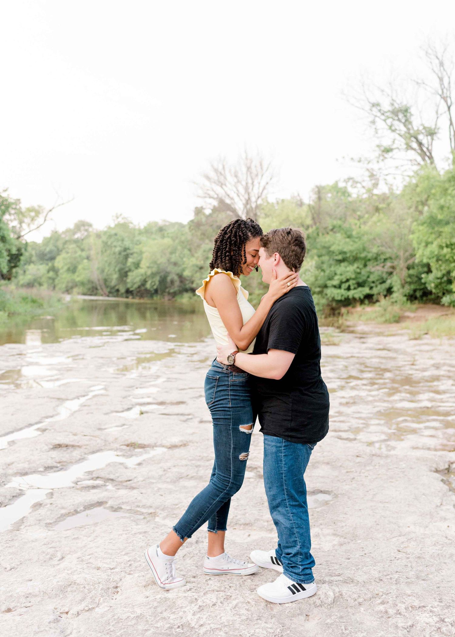A couple shares an intimate moment while standing on rocky terrain near a river.