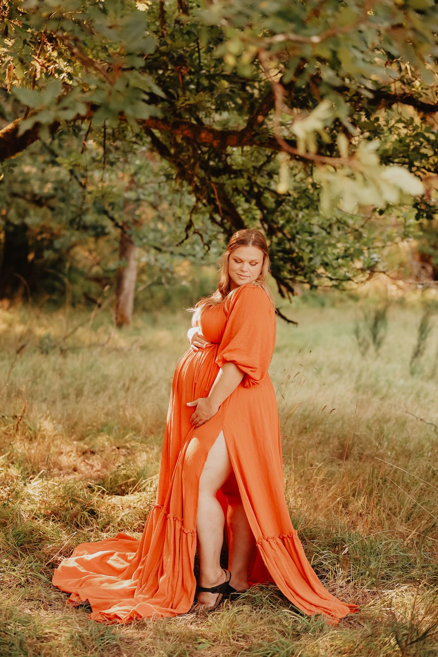 Flowing orange dress in autumn field with golden light filtering through trees.