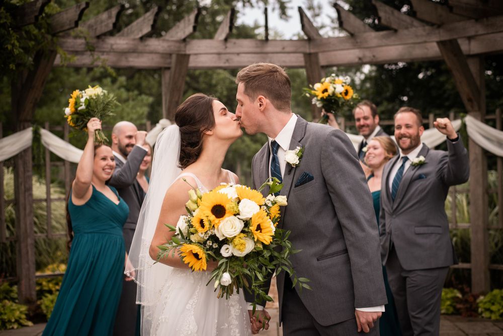 Bride and groom kissing with wedding party cheering at Stratford Country Club wedding