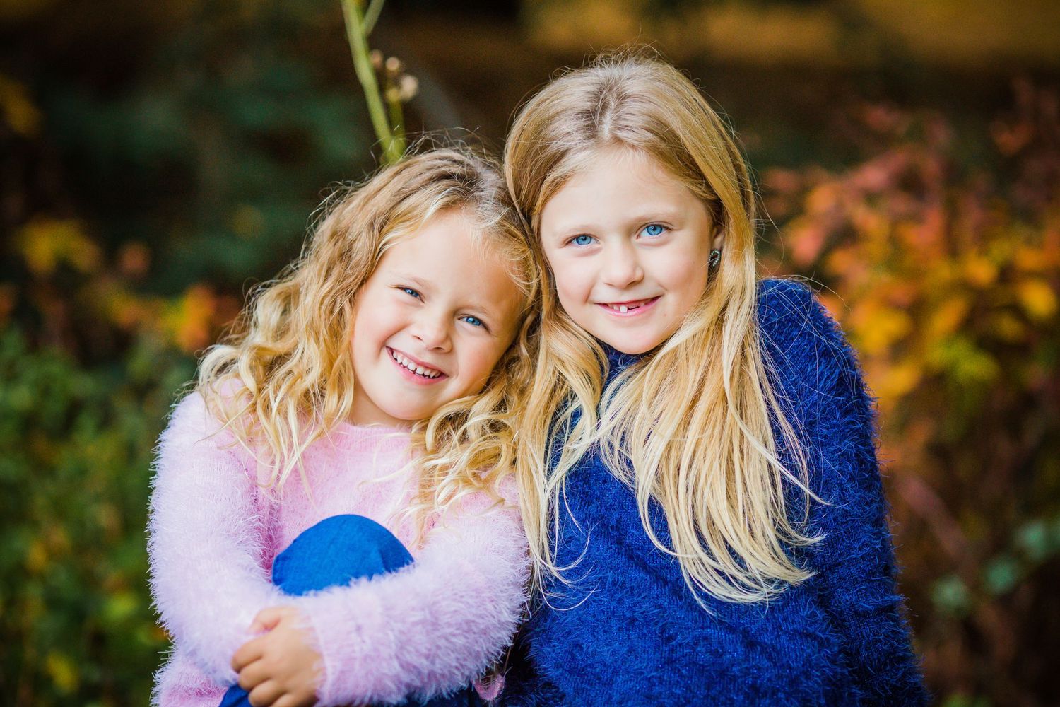 Two young siblings in cozy sweaters share a happy moment against a backdrop of fall foliage.