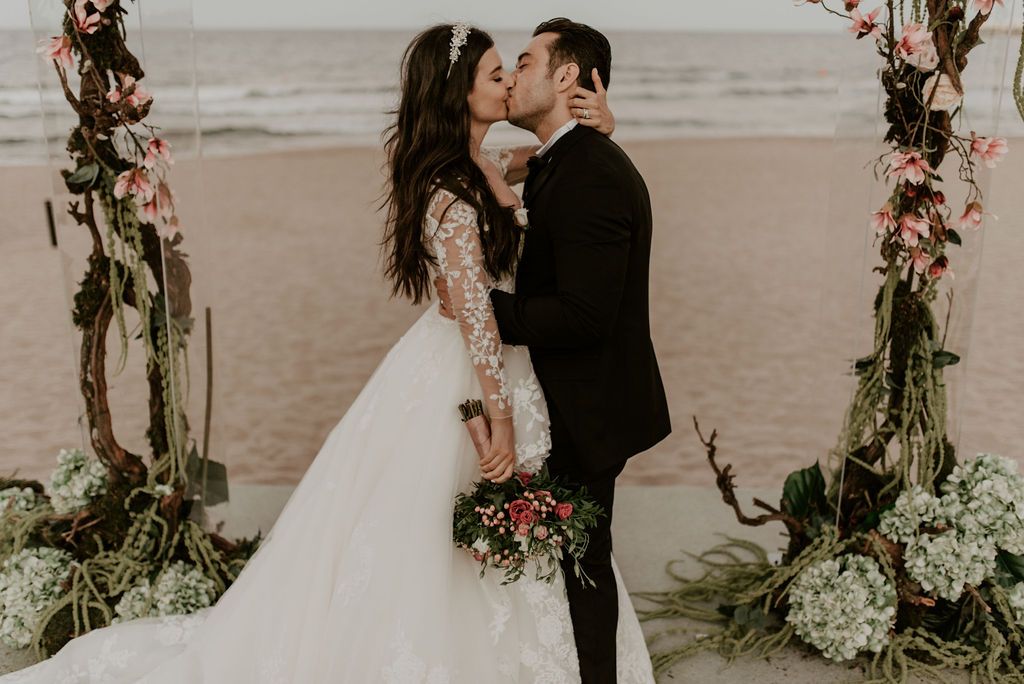 A romantic beach wedding ceremony setup with floral arrangements and an arch against the ocean backdrop.