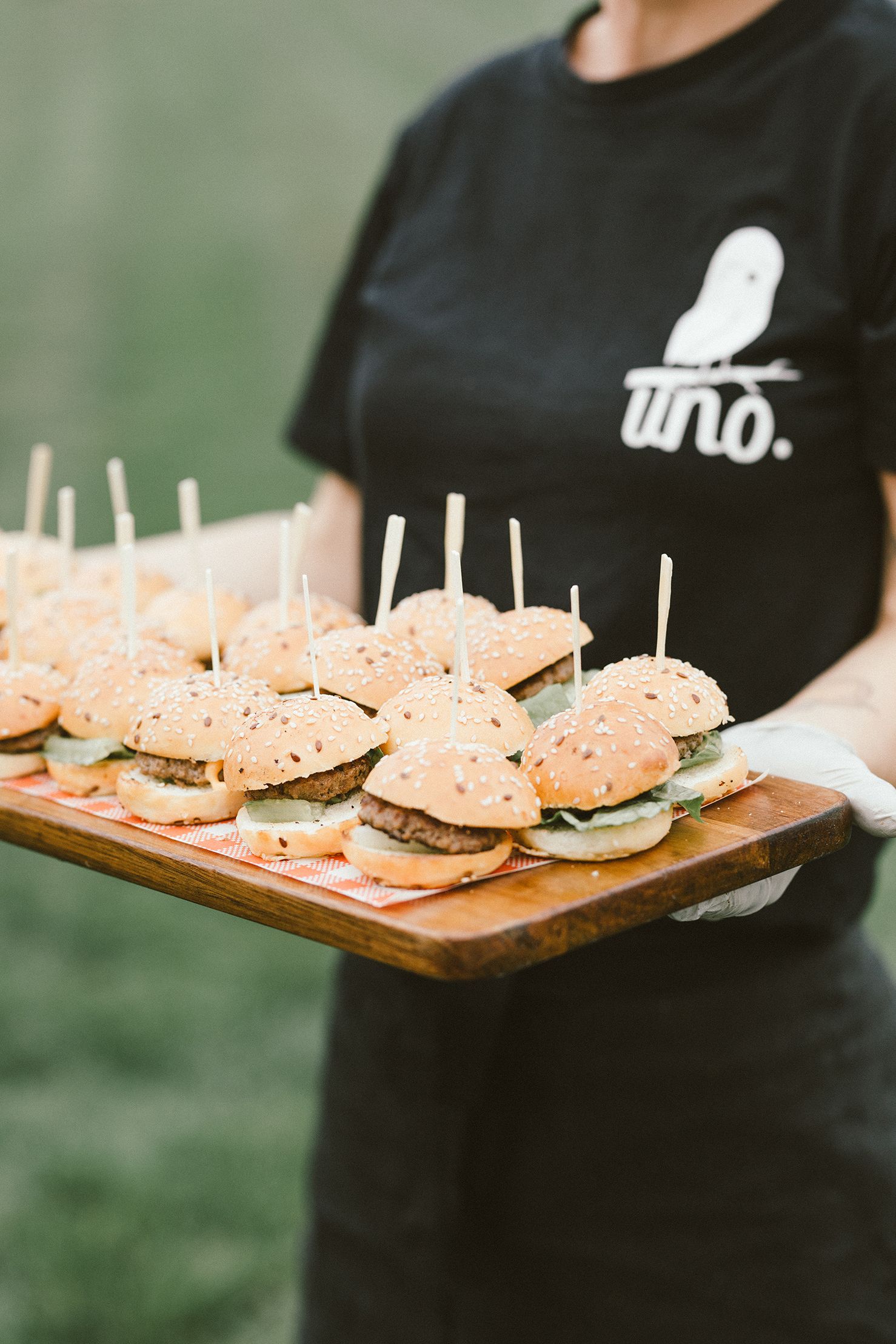 Wooden serving board with mini sliders topped with sesame seed buns being presented.
