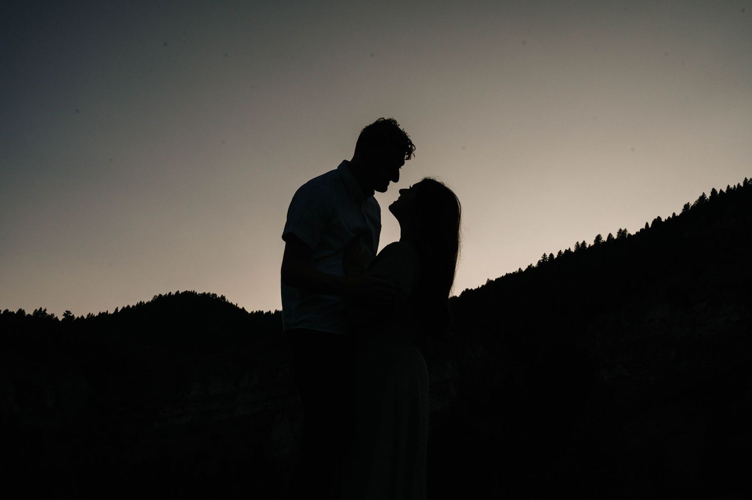 Silhouetted couple sharing intimate moment against sunset mountain landscape.
