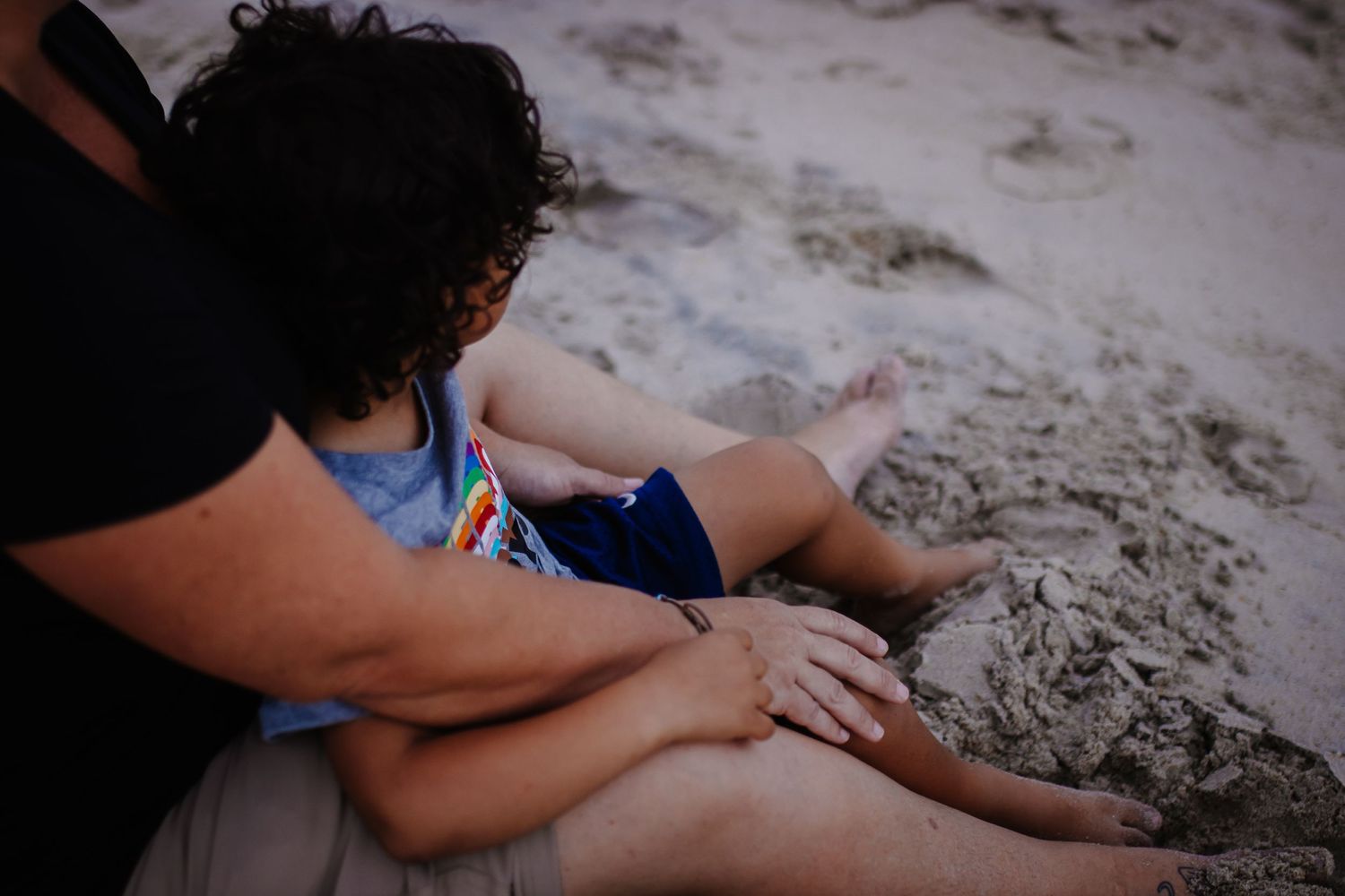 A child playing in the sand at the beach while being supervised.