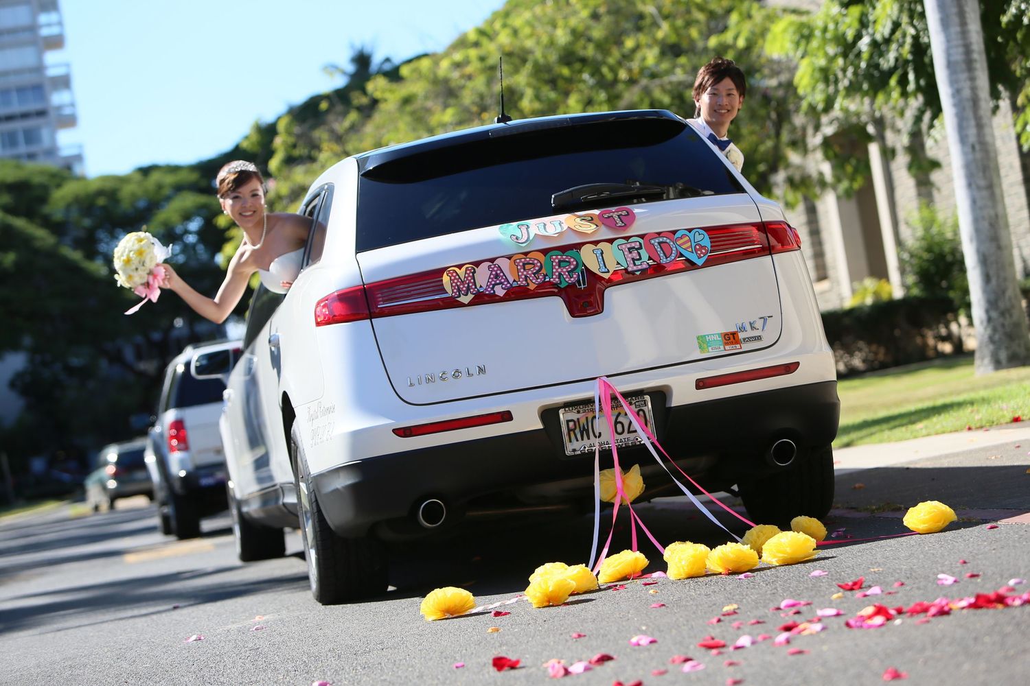 Newlyweds posing beside decorated white SUV wedding car with colorful signs and lemons.
ハワイウェディング
ハワイ挙式