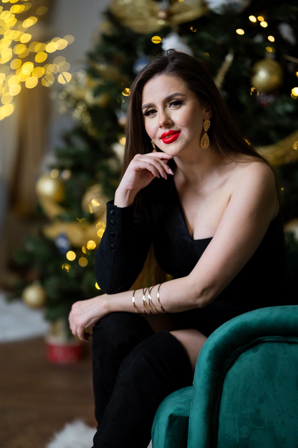 Dramatic holiday portrait on emerald velvet couch with bokeh lights in background.