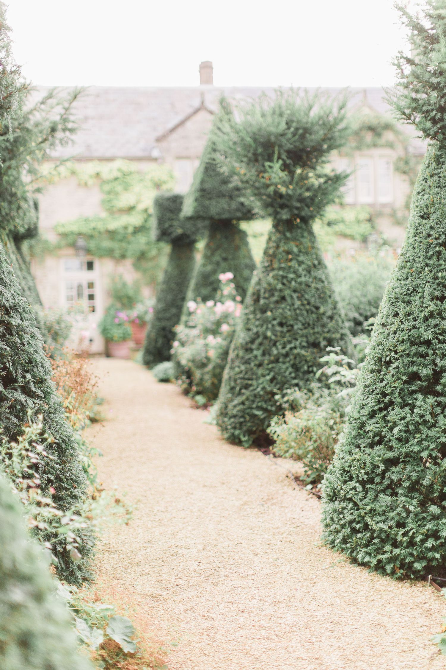 A serene garden path lined with manicured topiary evergreen trees leads to a charming countryside cottage euridge manor