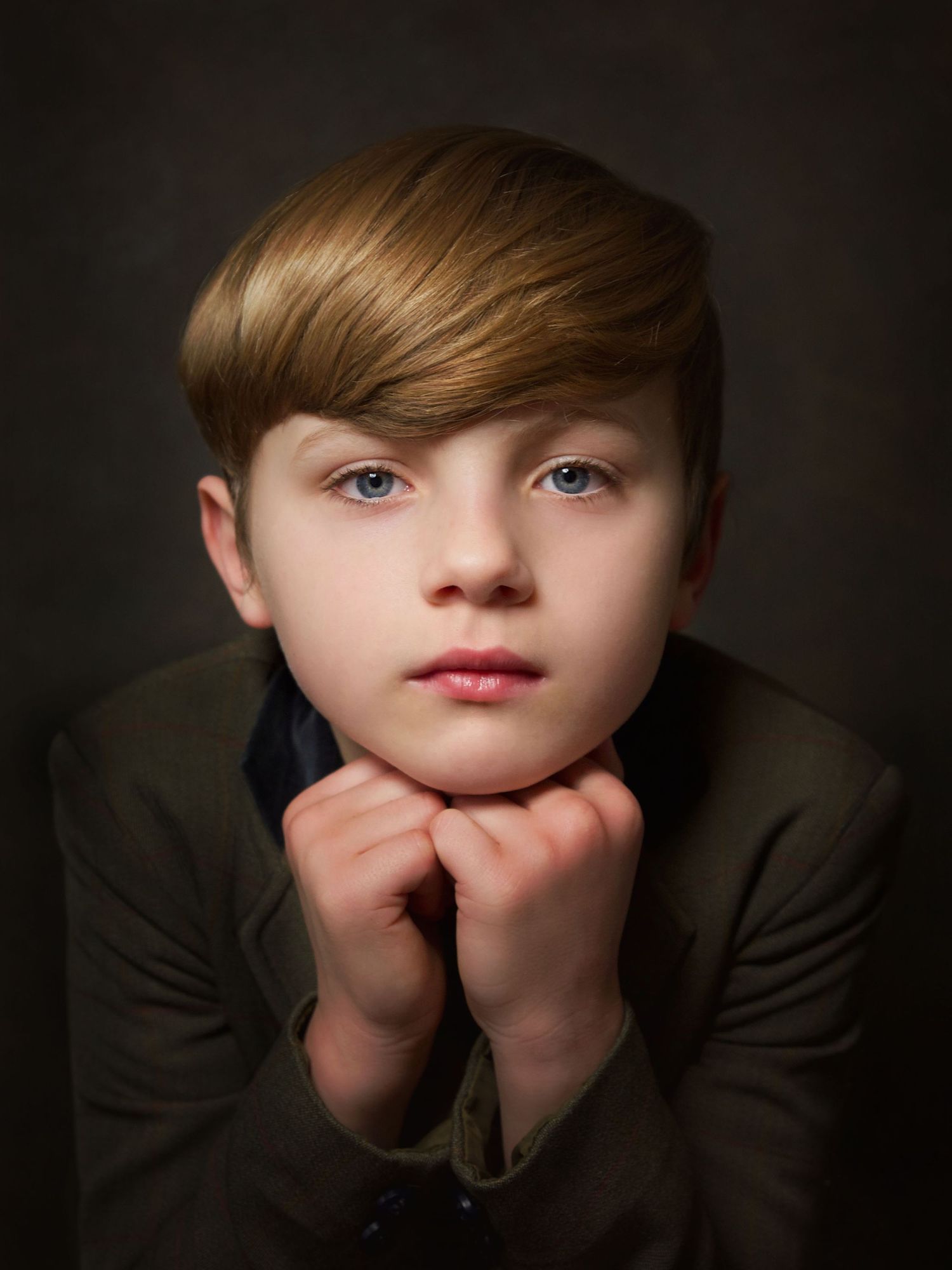 portrait of a young boy wearing jacket holding hands together under his chin