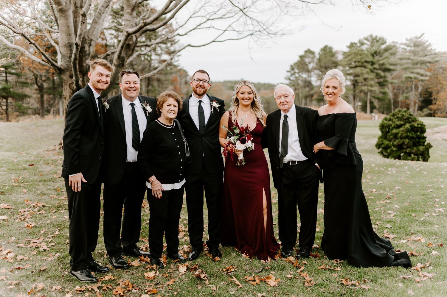 A formal group photo of wedding party members dressed in black and burgundy attire.